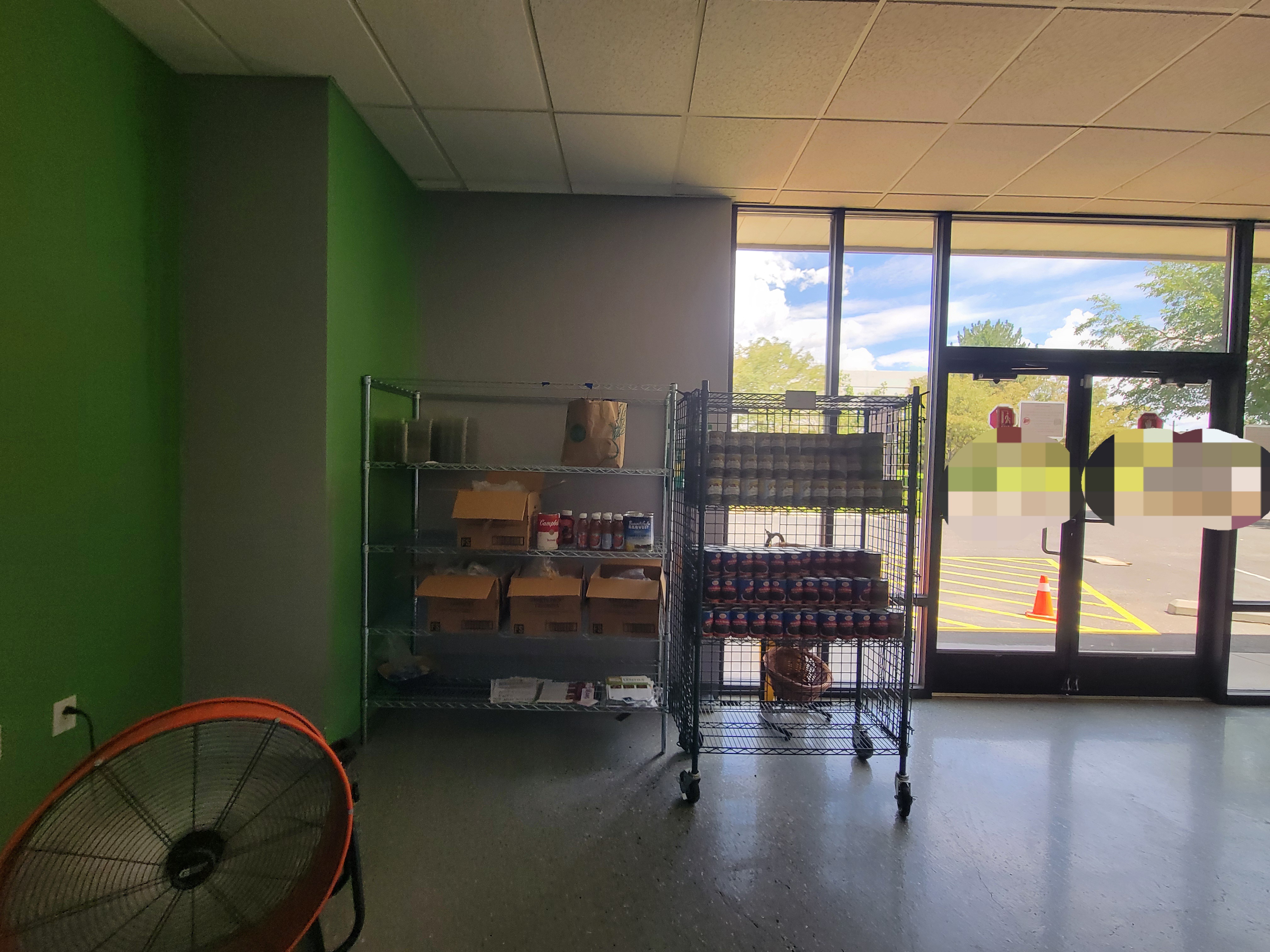 Food on shelves next to glass doors and a fan in front of it.